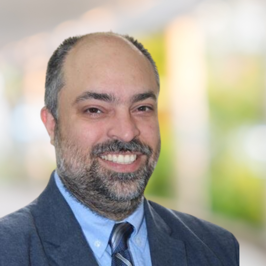 Headshot of Dr. Behrouz Bakhtiari, a smiling man with a beard, wearing a blue shirt and a patterned tie.