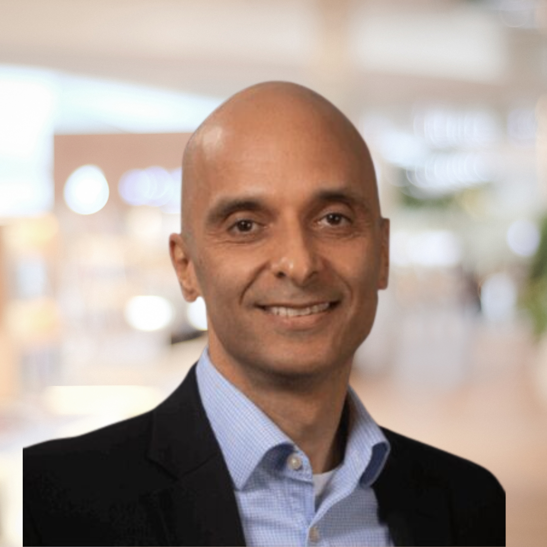 Headshot of Dr. Sash Vaid, a smiling bald man wearing a blue shirt and black suit jacket.
