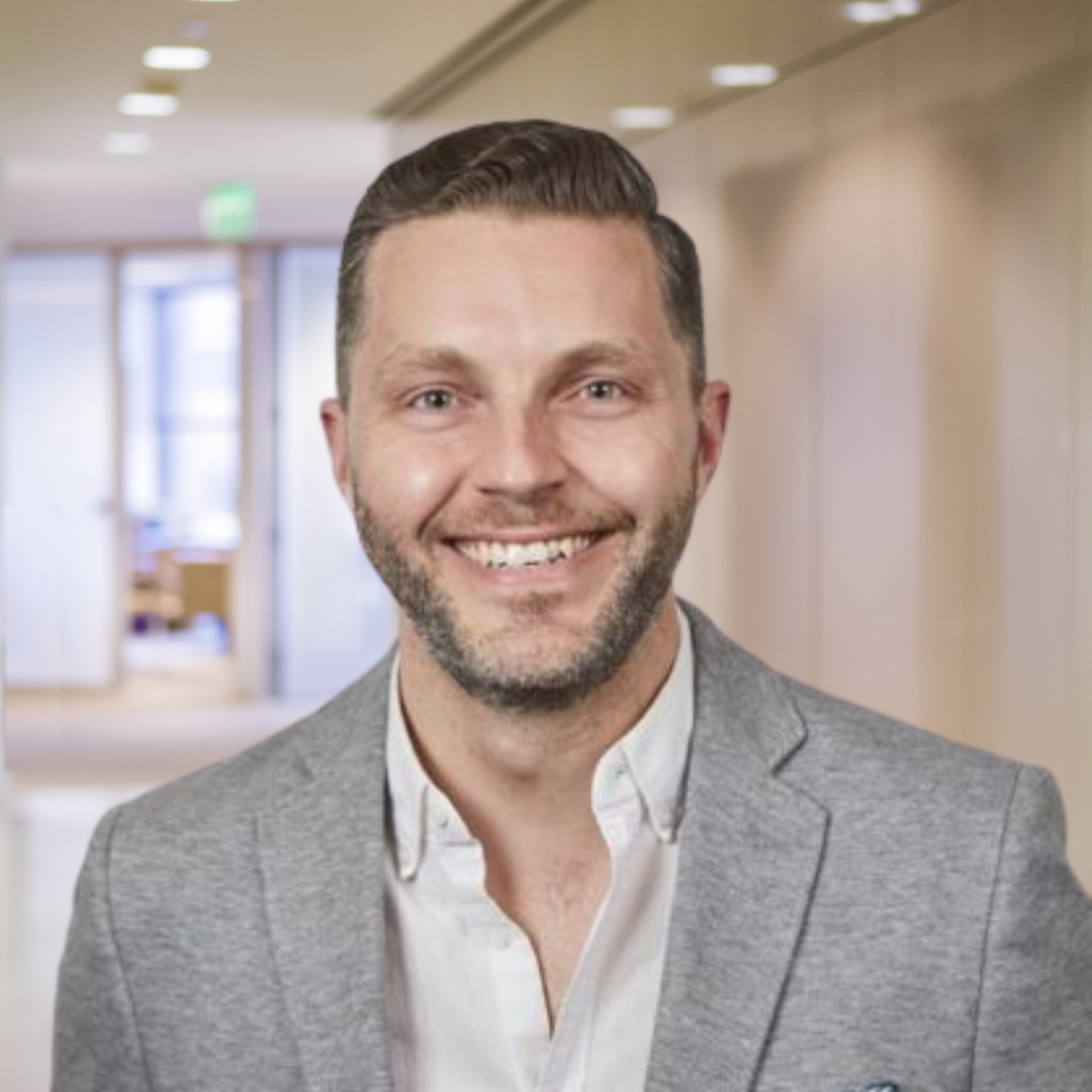 Headshot of Dr. Shane Saunderson, a smiling man with a beard, wearing a white shirt and a light grey jacket.